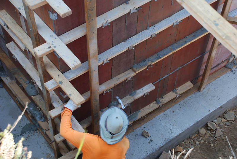 A small amount of concrete can be seen leaking between the form panels, so a concrete worker is tapping the joints to tighten them.