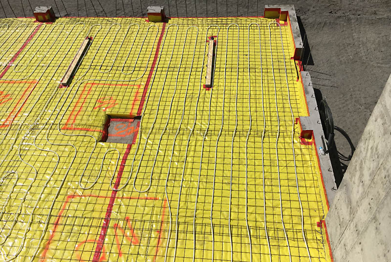 This is a picture of the SW corner of the garage floor before the concrete slab was poured. The level inside the foundation was brought up with compacted structural fill, then gravel was used to create a base for the concrete. A 6" pipe with air vents is buried around the inside perimeter of the foundation within the gravel for a future radon gas venting system if one is required. Two inch thick blue foam is sitting on top of the gravel, then a 15–mil yellow polyethylene vapor barrier covers that and is sealed with red tape. Six–inch welded wire fabric is placed to reinforce the slab, then Pex tubing for raidant heat is secured to the wire with ties.