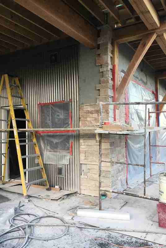 Masons applied a thin stone veneer to the face of the garage, wrapping about 30" onto the carport walls. The wall was prepared for stone by covering it with tar paper and stapling aluminum lath to the face. A scrim coat of mortar was applied, then the stones were adhered to that base with additional mortar. The stone is locally sourced Colorado Buff sandstone with mineral staining and it's about 2½" thick.