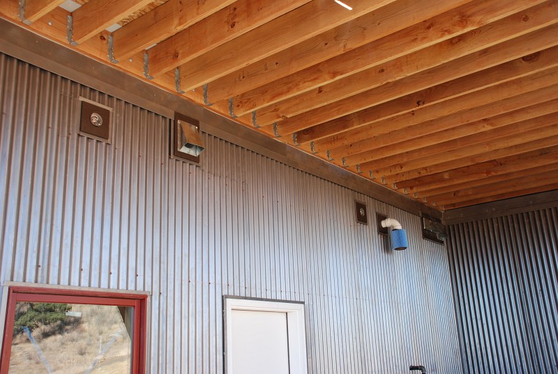 This close up of the east carport shows the 1½" thick cedar pads I built to create a flat surface for the lighting fixtures and ducts that penetrate the corrugated steel. The blue filter is a HEPA vacuum cleaner filter I fitted to the boiler intake to keep construction dust out.