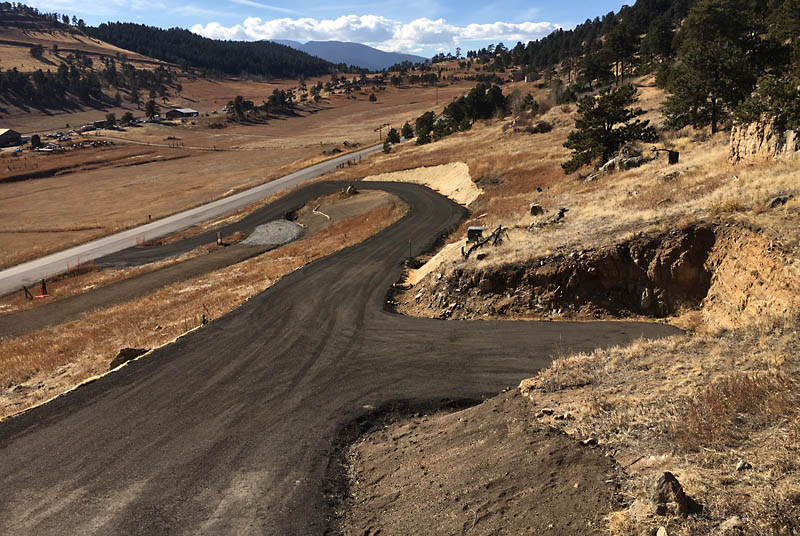 Here is a view of the driveway and hammerhead as seen from the west deck. Recycled asphalt was placed and compacted to provide a hard surface that resists erosion and creates little dust. In addition, the dark color will accelerate snow melt in the winter time to help keep the driveway clear.