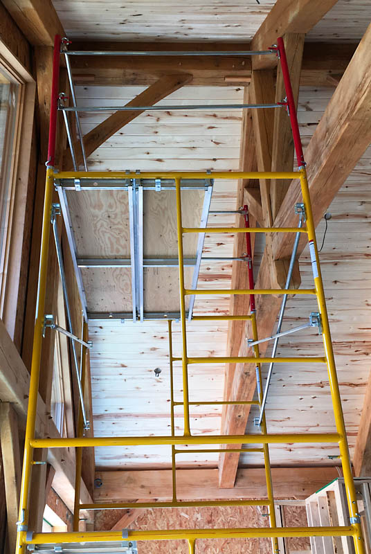 We purchased our own scaffolding to access the vaulted ceiling in the living room. Here, the scaffolding is set up with two six foot frames and a guard rail in red: with the 8" casters, this puts the top platform about 13 feet up in the air. I add a final four foot frame to get to the ridge beams.