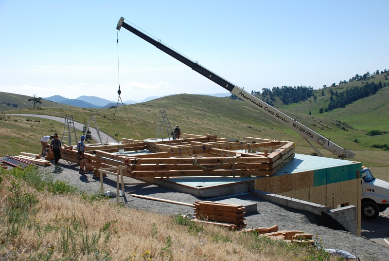 The crane is lifting the post and beam assembly that is part of the east carport. Bents 6, 5 and 4 have been preassembled on the deck and await the crane. 