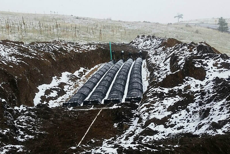 Here is the leach field system installed. Graded sand has been used to backfill the trench, then a long pipe with sprinkler nozzles is suspended under each row of the half-dome plastic covers. This is the latest technology in drain fields and is replacing the perforated drain tile used in the past.