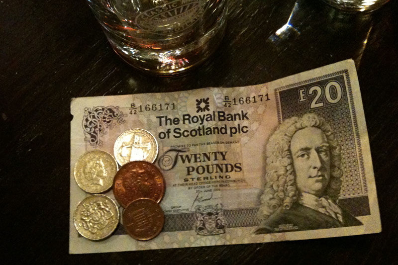 <h3>Miscellaneous Items</h3>The British Pound Sterling is used throughout the United Kingdom. Paper notes are issued by the Bank of England, or — like this one — by one of three banks in Scotland. This denomination is notable because it features Adam Smith (economist), rather than the Queen of England. The three gold–coloured coins are £1. The large copper coin is two pence and the small copper coin is a penny.